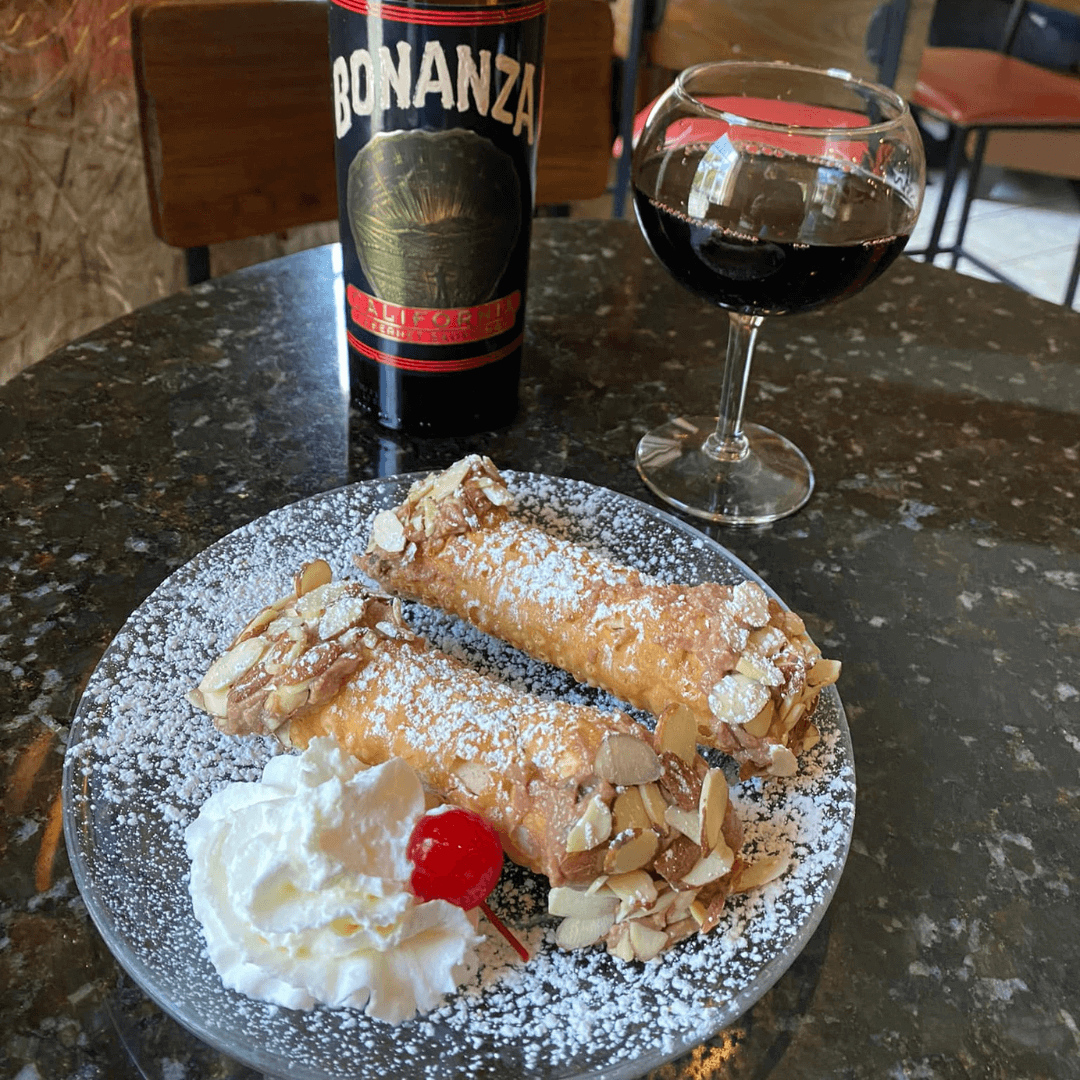 two cannoli's on a plate with a glass of wine